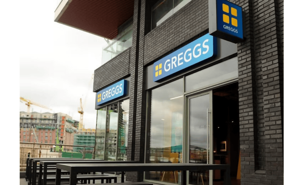 The shop front of Greggs in Titanic Quarter. Grey bricked building, glass door and Greggs signage